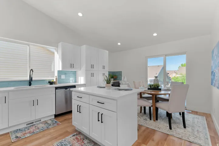 Open-concept kitchen featuring white shaker cabinetry, an island with a solid surface countertop, wood-finish flooring, a stainless steel dishwasher, and a glass tile backsplash