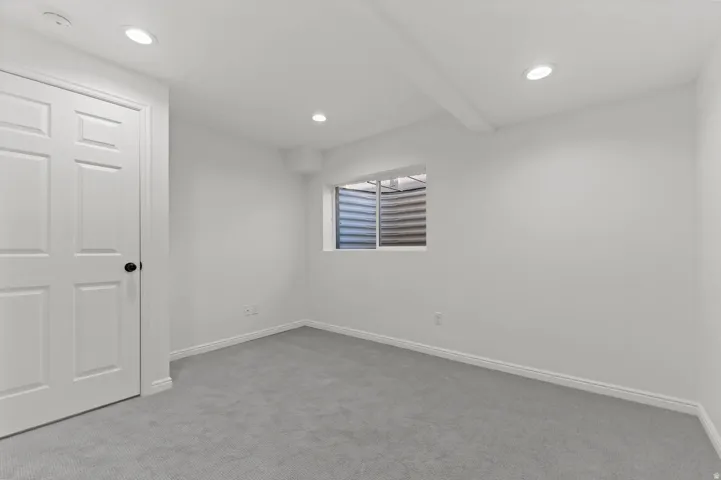 Neutral-toned room featuring light gray carpeting, white walls, and a white six-panel door with black hardware