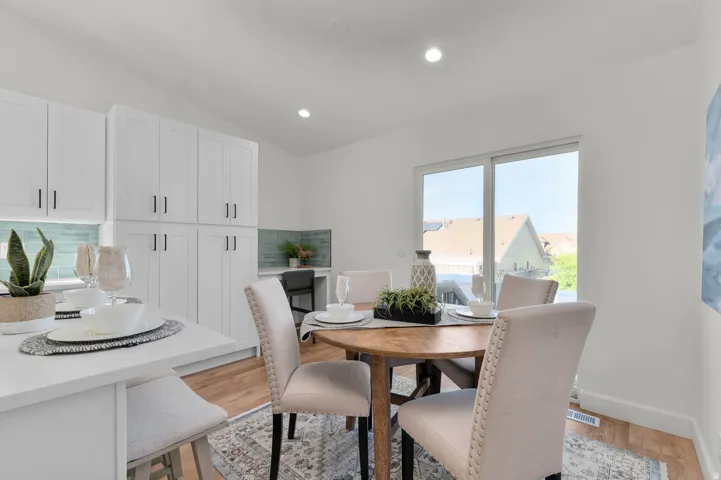 Open-concept kitchen and dining area featuring white cabinetry, a built-in desk area with a tiled backsplash, and wood-finish flooring