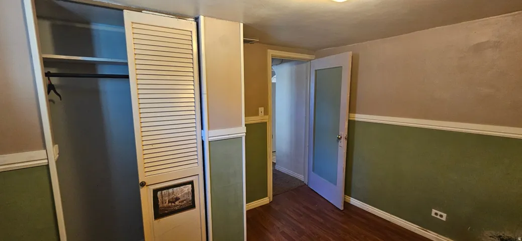 Room featuring wood-finish flooring, two-tone wall treatment with wainscoting, and a built-in closet with louvered bifold doors