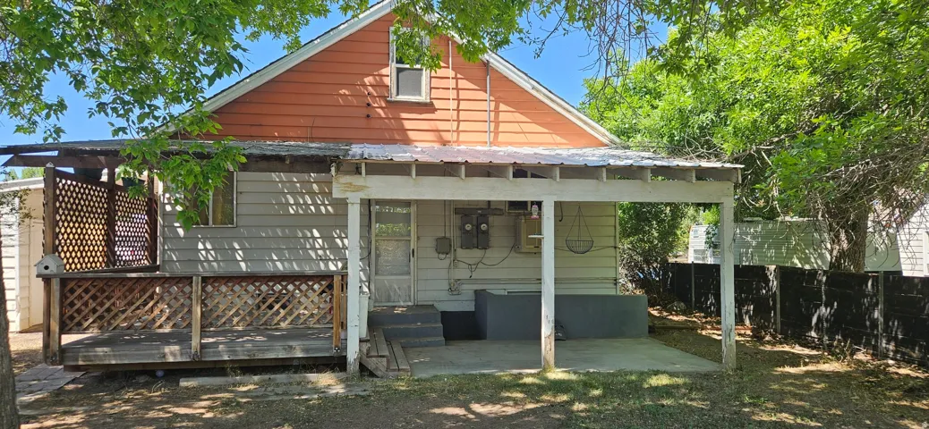 Rear exterior featuring a covered patio, adjacent wood-decked area with lattice railing, and a windowed gable end
