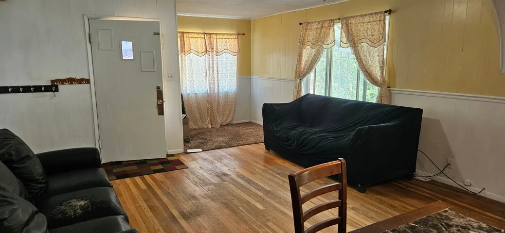 Living area featuring wood-finish flooring, two large windows, wainscoting, and a paneled accent wall