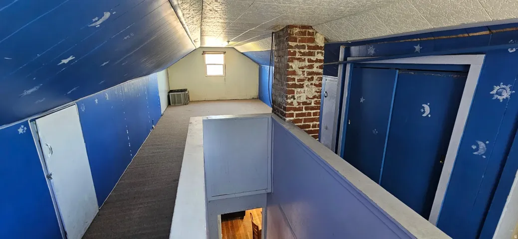 Upper-level loft space featuring a brick chimney, a window, and sloped ceilings