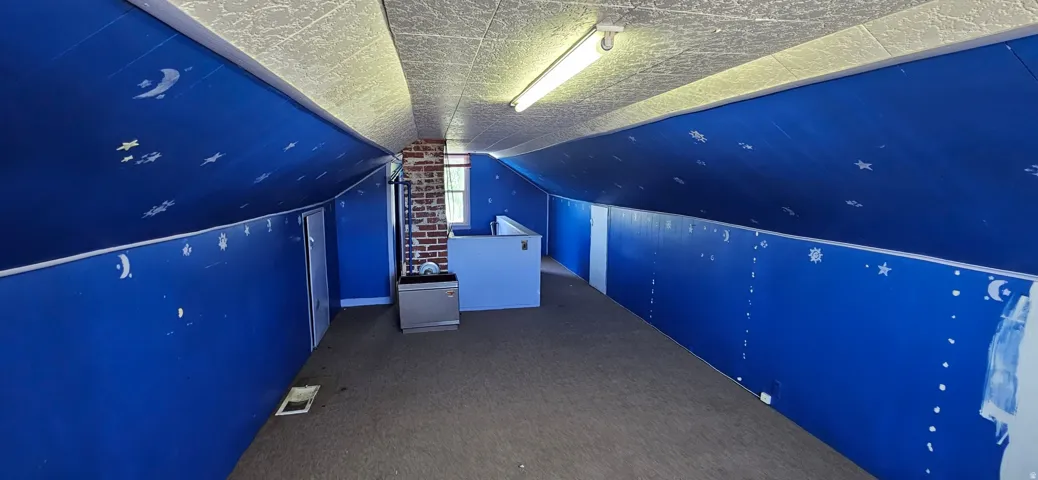 Carpeted attic space with sloped blue walls, a textured ceiling, exposed brick chimney, and a single window