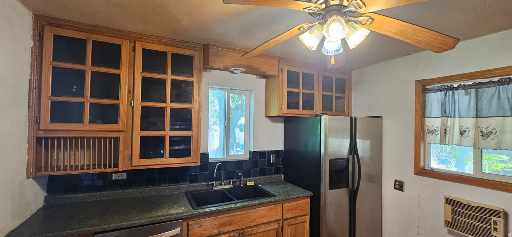 Kitchen featuring wood cabinetry, a double basin sink, black tile backsplash, and a stainless steel refrigerator
