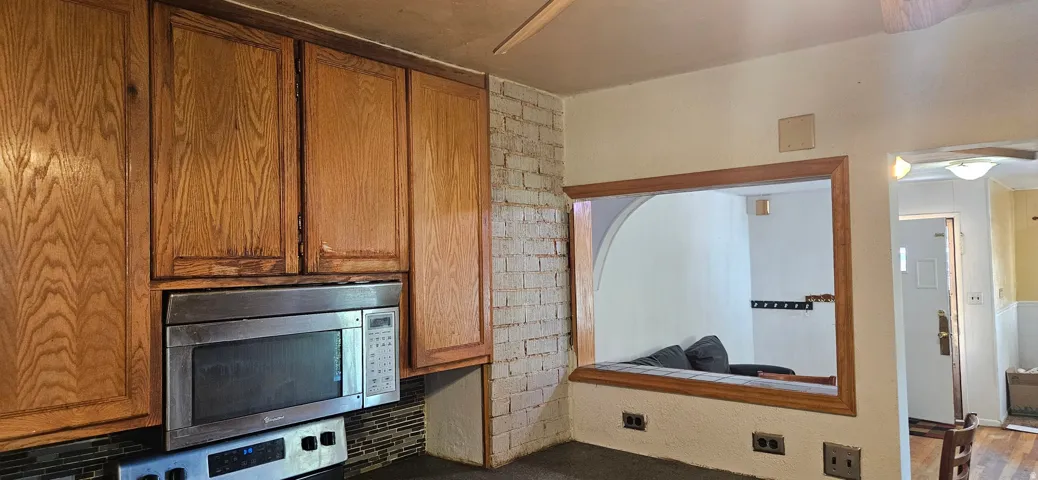 Kitchen featuring wood cabinetry, stainless steel over-the-range microwave, mosaic tile backsplash, and a pass-through opening with wood trim
