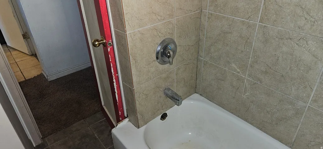 White bathtub with tile surround, chrome fixtures, and a brass-finished doorknob