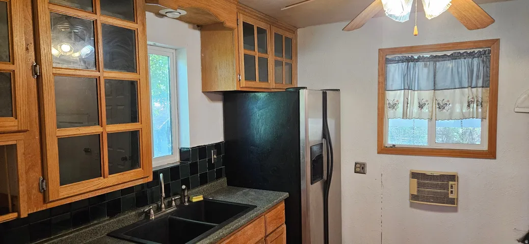Kitchen featuring wood-finish cabinetry with glass panel doors, dark countertop, and a double basin sink