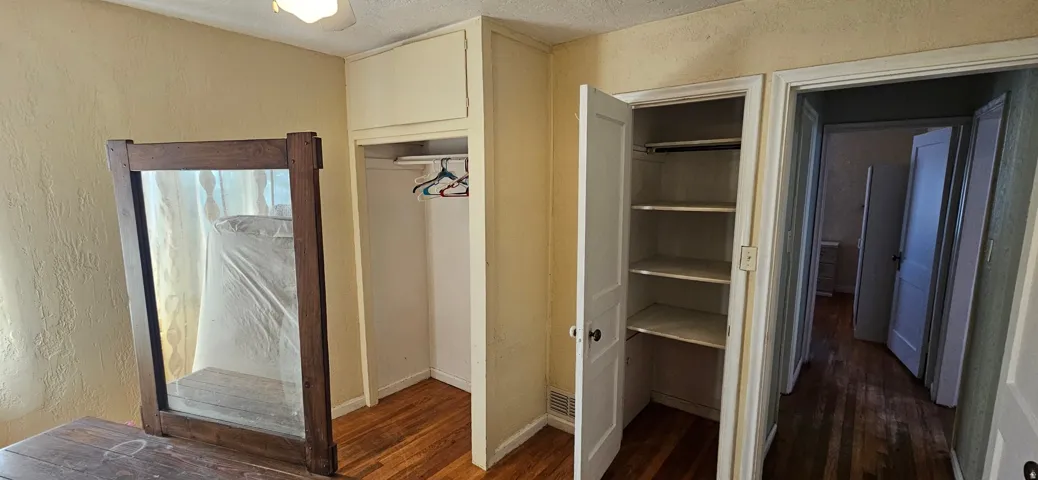 Bedroom featuring wood-finish flooring, a built-in closet with an overhead cabinet, and an additional built-in storage cabinet with shelving