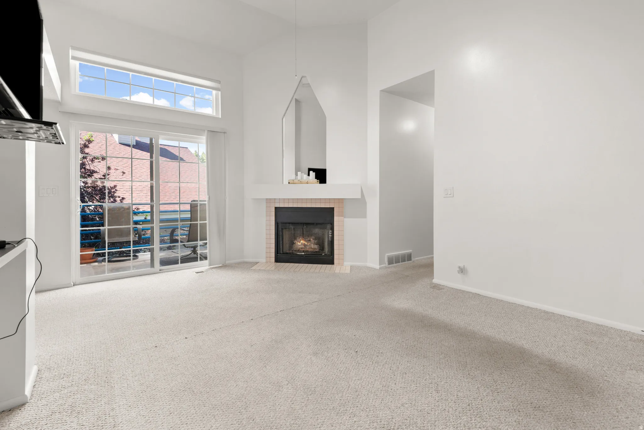 Living area featuring vaulted ceilings, a fireplace with a light-colored mantel and hearth, and light-toned carpeting