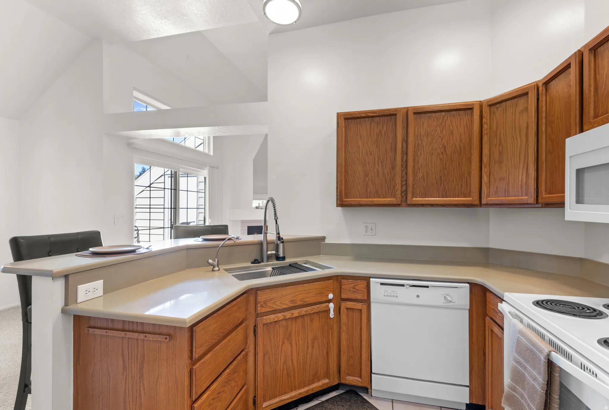 Kitchen featuring wood cabinetry, light-toned countertops, and white appliances including a built-in microwave and dishwasher
