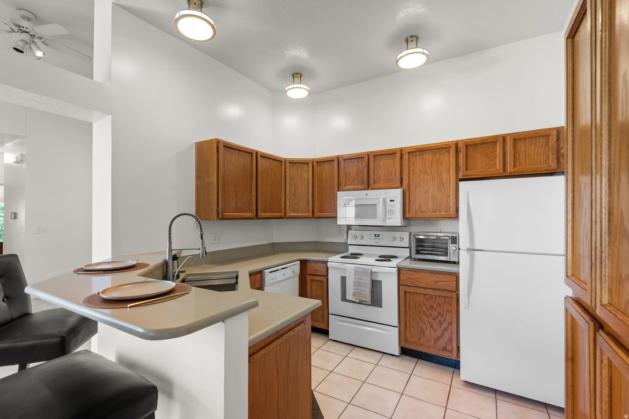 Kitchen featuring wood cabinetry, light-toned countertops, tile flooring, and white appliances