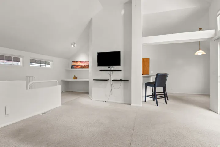 Carpeted loft space featuring an open railing, built-in desk with shelving, and recessed lighting