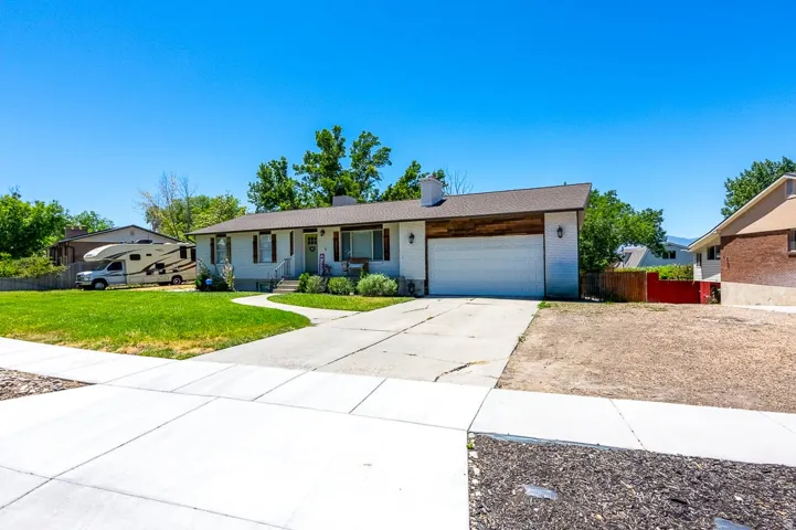 Single-story residence featuring a two-car garage with a wood-finish accent panel, a paved driveway, and a front walkway