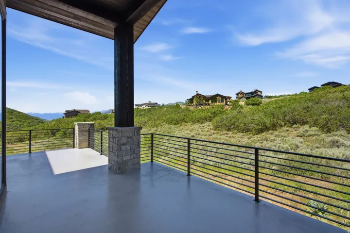 Covered outdoor deck with a smooth gray surface, featuring a horizontal bar railing system and stone-clad columns