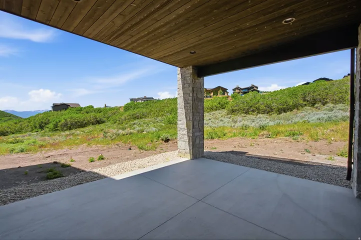 Covered patio featuring a concrete surface, stone-clad columns, and a wood-finish ceiling with recessed lighting, overlooking a natural hillside landscape