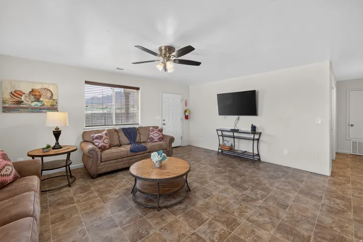 Spacious living area featuring tiled flooring, a ceiling fan, and a window with horizontal blinds