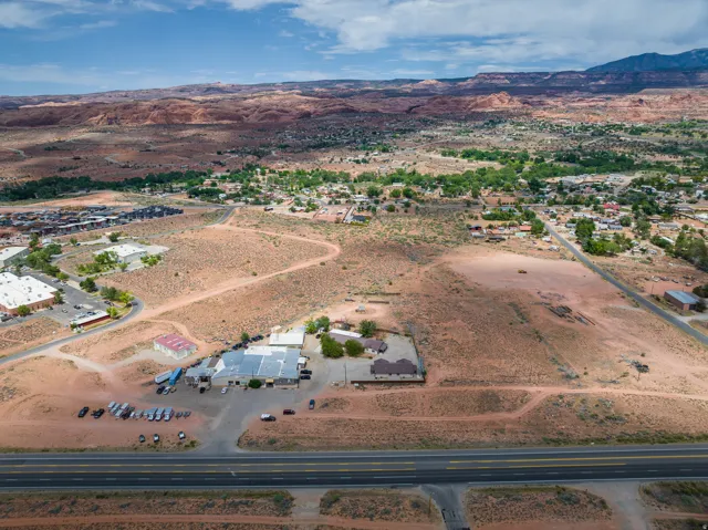 Expansive arid landscape featuring scattered buildings, a prominent multi-lane roadway, and distant mountain formations