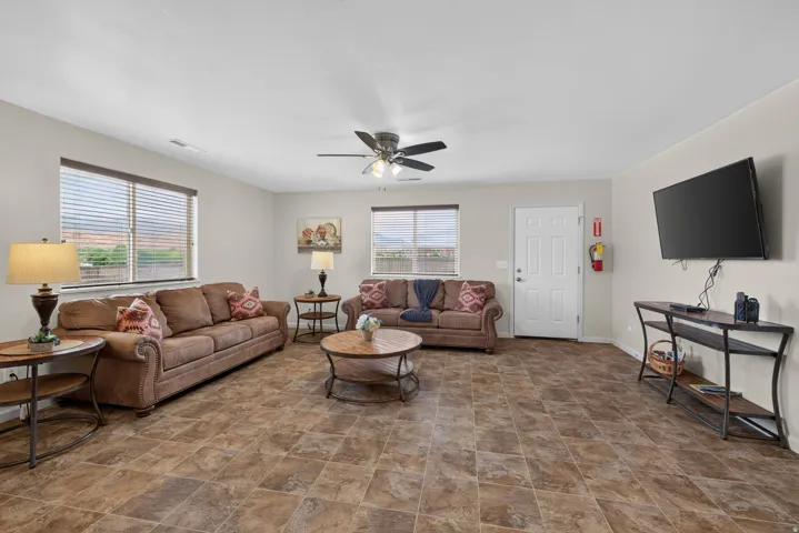 Spacious living area featuring multi-toned tile flooring, neutral wall paint, and multiple windows with horizontal blinds