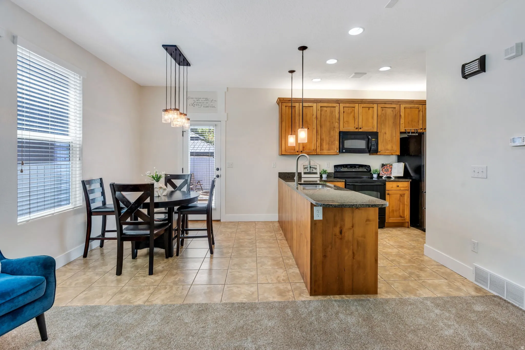Open-concept kitchen and dining area featuring warm-toned cabinetry, a spacious island with a stone-finish countertop, and tile flooring