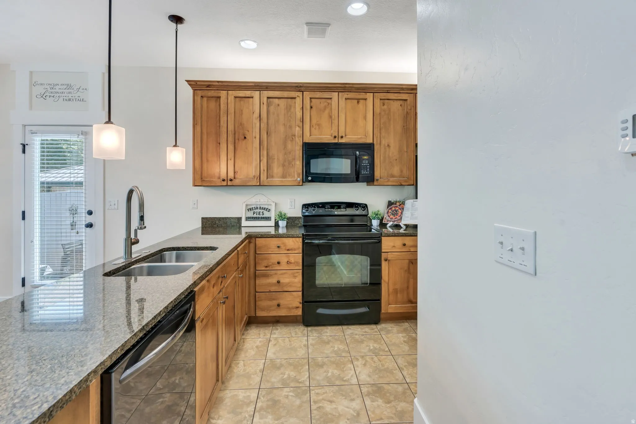 Kitchen featuring wood cabinetry, granite-style countertops, stainless steel dual basin sink with gooseneck faucet, black oven range, and built-in microwave