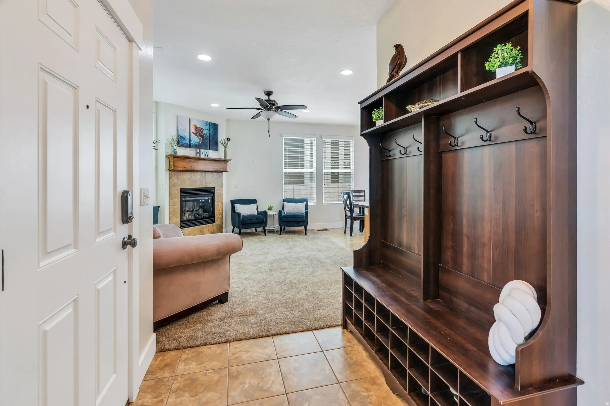 Entryway featuring a built-in dark wood-finish hall tree with storage cubbies and coat hooks, opening into a living area with a fireplace and ceiling fan