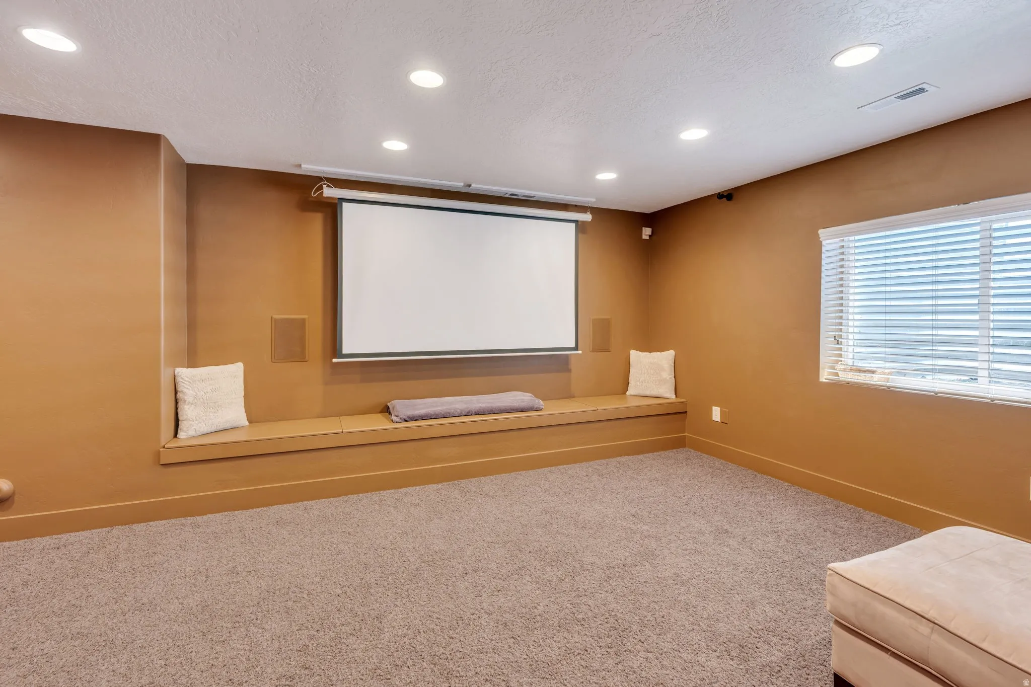 Entertainment room featuring a retractable projector screen, integrated speakers, a built-in bench seat, recessed lighting, and soft carpeting