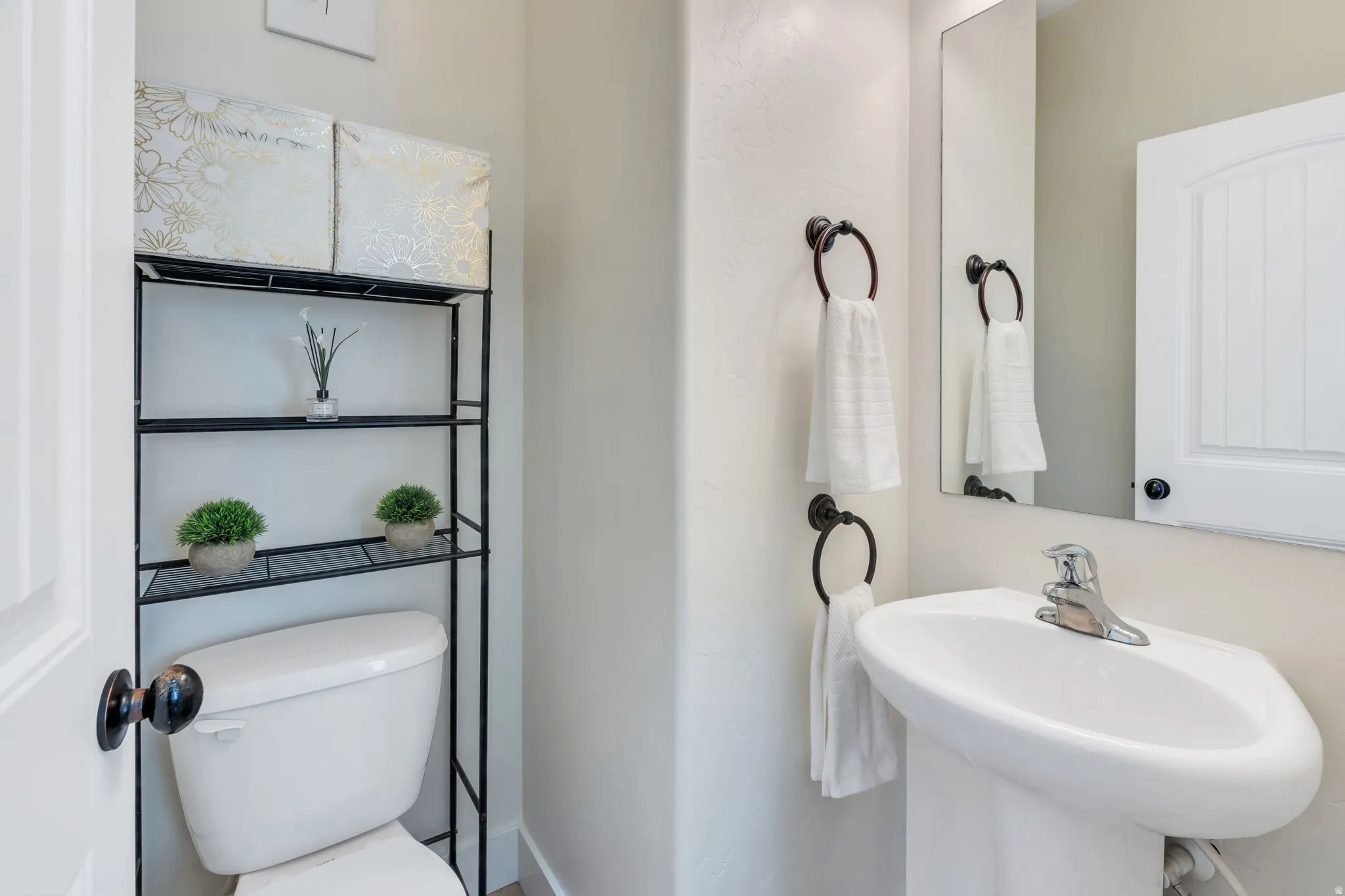 Pedestal sink with chrome faucet, wall-mounted mirror, and black towel rings