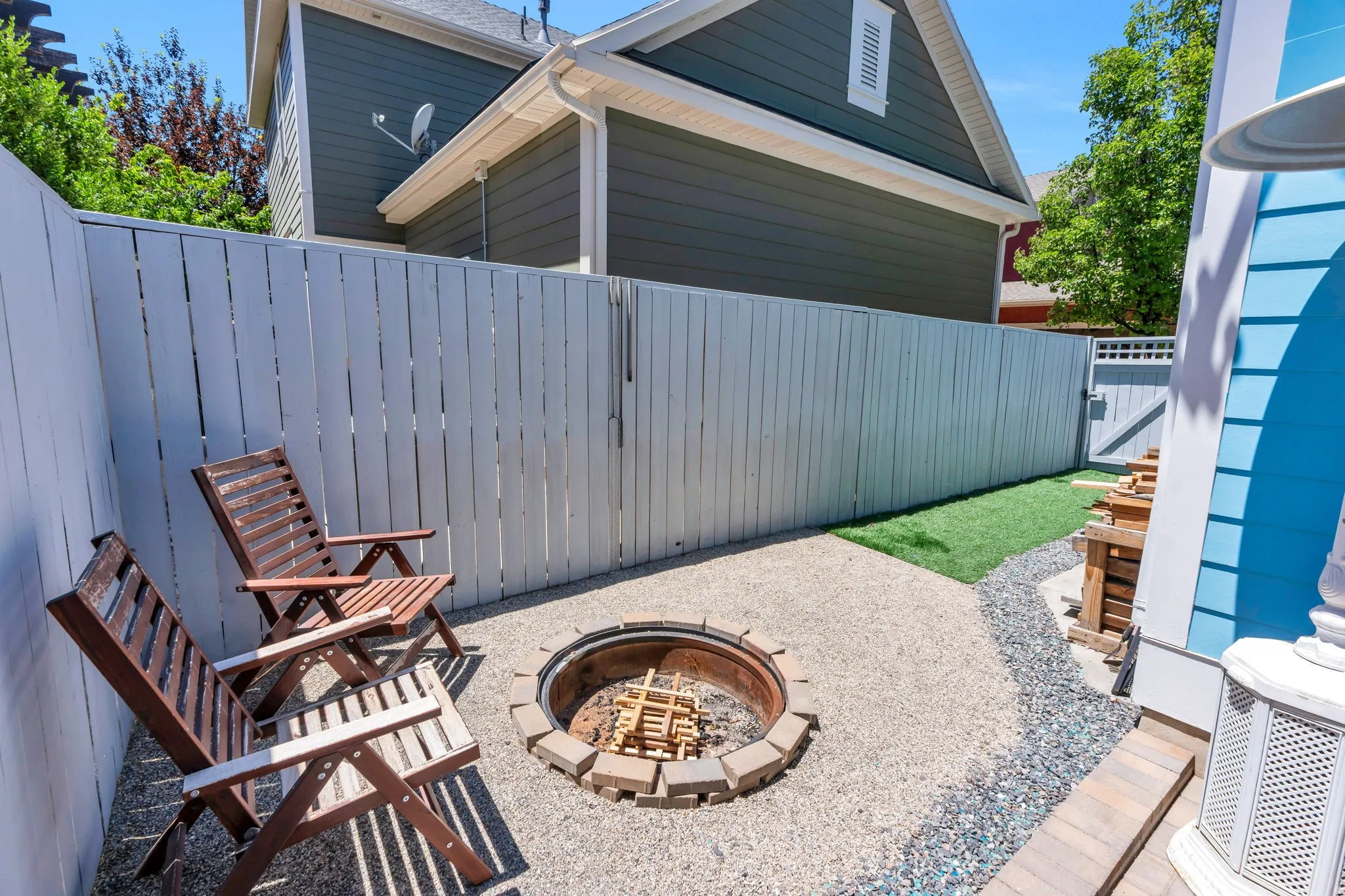 Outdoor patio space featuring a built-in fire pit with stone surround, gravel flooring, and a strip of artificial turf