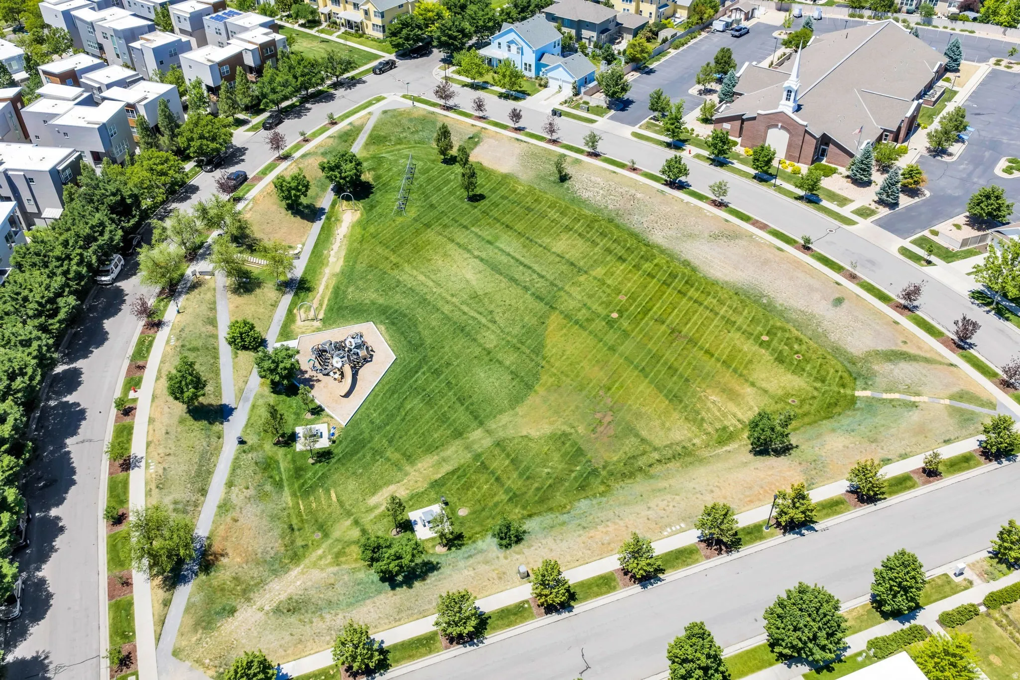 Expansive green space featuring a playground area, paved walking paths, and mature trees
