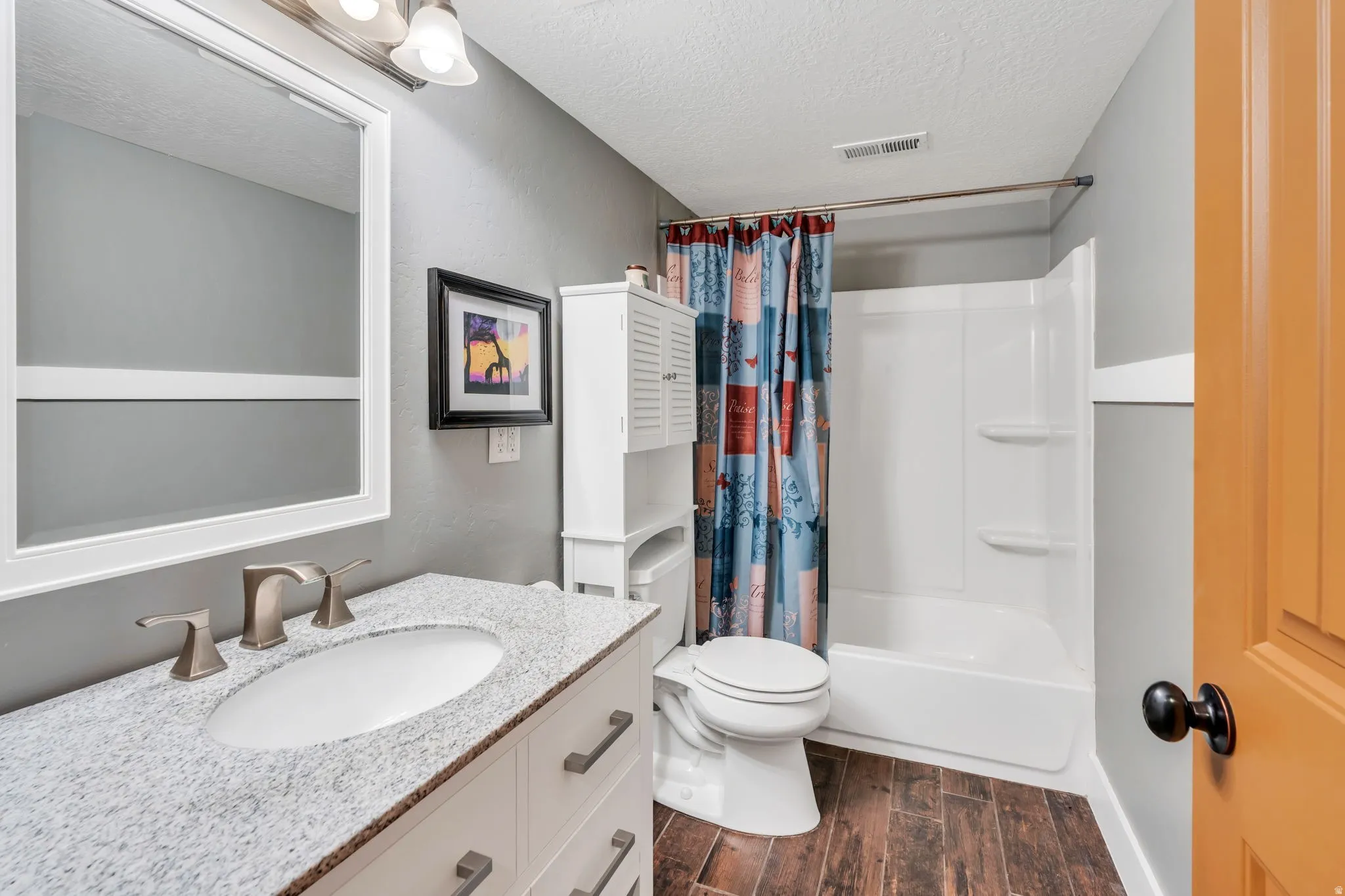 Bathroom featuring a white vanity with a light speckled countertop, wood-finish flooring, and a white shower-tub combination