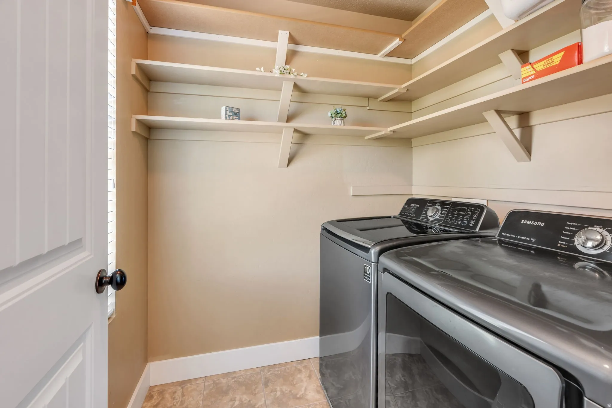 Utility area featuring extensive built-in shelving, durable flooring, and a paneled door with matte black hardware