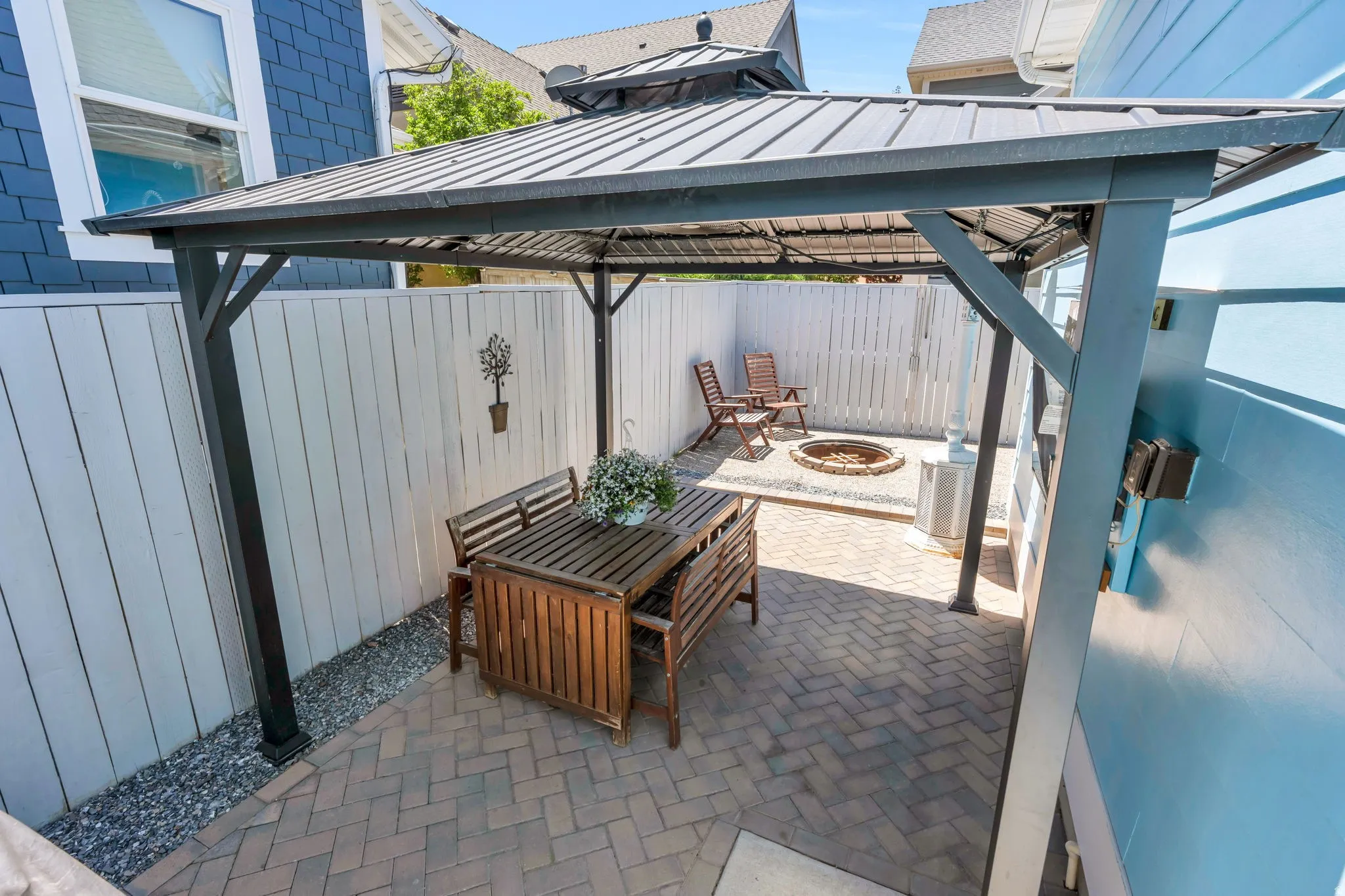 Outdoor patio featuring a metal gazebo, paver flooring, a white privacy fence, and a built-in fire pit