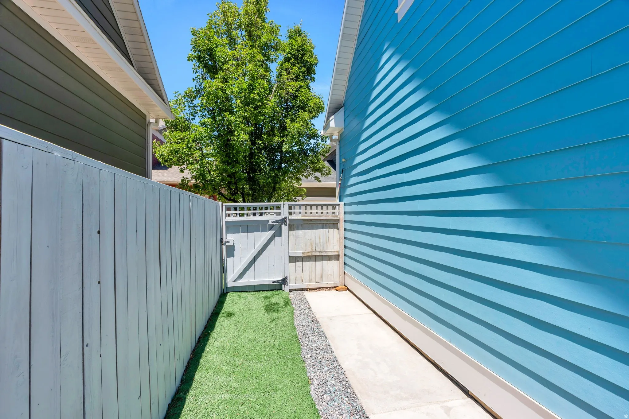 Side yard with a light gray wood fence, artificial turf, and a concrete walkway