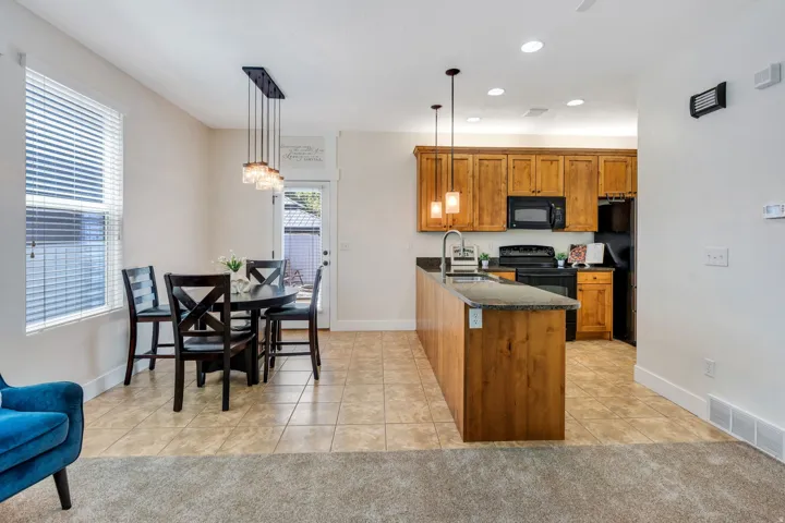 Open-concept kitchen and dining area featuring warm-toned cabinetry, a spacious island with a stone-finish countertop, and tile flooring