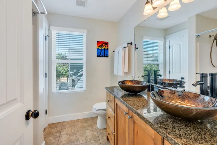 Bathroom featuring a dual vanity with vessel sinks, a granite countertop, wood cabinetry, and tiled flooring