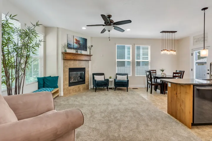Living area featuring a tiled fireplace with a wood mantel, a ceiling fan with light fixture, and multiple windows with blinds