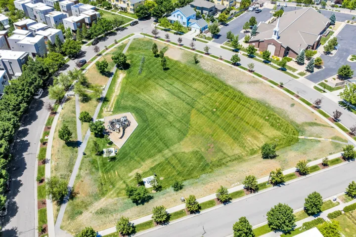 Expansive green space featuring a playground area, paved walking paths, and mature trees