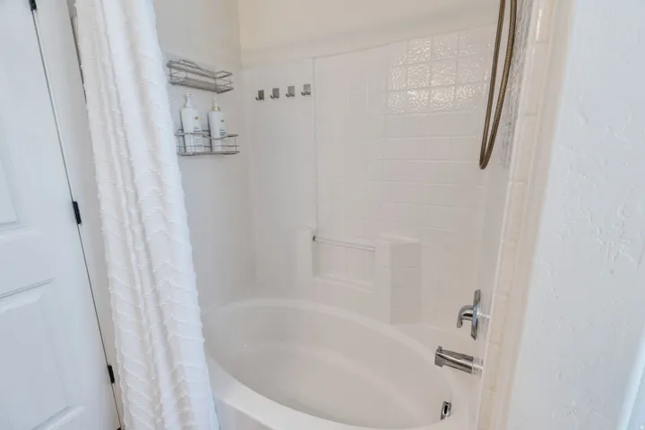 Bathtub with white tile surround, chrome fixtures, and built-in shelving