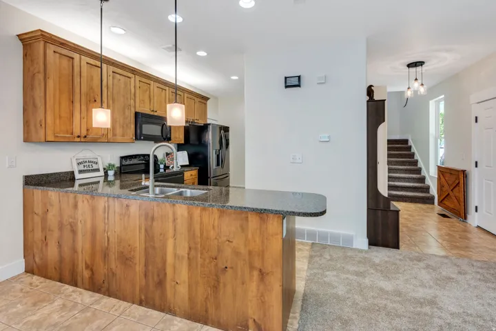 Kitchen featuring granite countertops, wood cabinetry, stainless steel sink with gooseneck faucet, black appliances, and recessed and pendant lighting