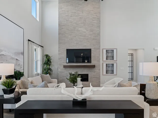 Two-story living area featuring a stone-clad fireplace surround with a dark wood-finish mantel, an integrated fireplace unit, and a high window offering natural light