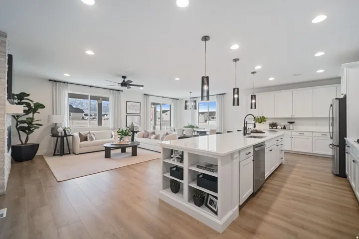 Open-concept living space featuring wood-finish flooring, a contemporary kitchen island with pendant lighting, white cabinetry, and recessed lighting throughout