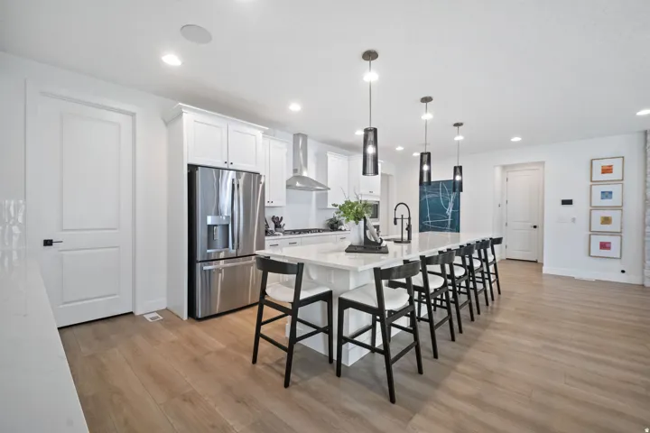 Open-concept kitchen featuring white cabinetry, stainless steel appliances, a large center island with pendant lighting, and light wood-finish flooring