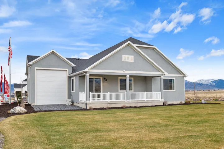 Contemporary stucco exterior featuring a covered front porch with white railing, an attached garage, and a spacious green lawn