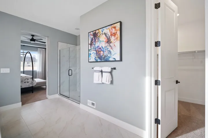 Spacious bathroom featuring large format tile flooring, a glass-enclosed shower with marble-look surround, and a door opening to an additional room with carpet flooring and shelving