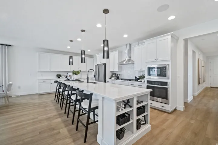 Spacious kitchen featuring a large central island with seating, white shaker cabinetry, stainless steel appliances, and wood-finish flooring