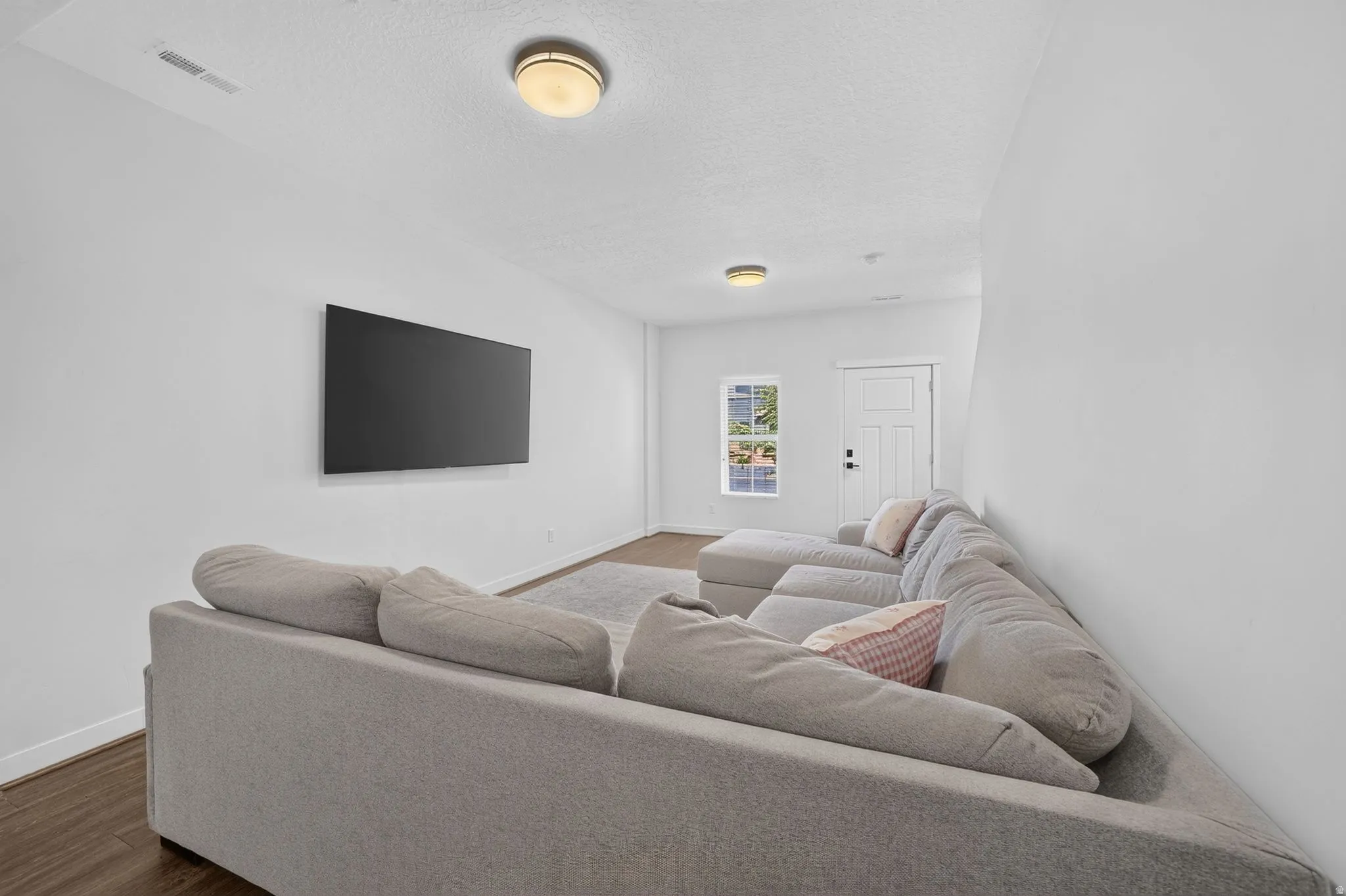 Bright, open room featuring a mounted flat-screen panel, wood-finish flooring, and white walls