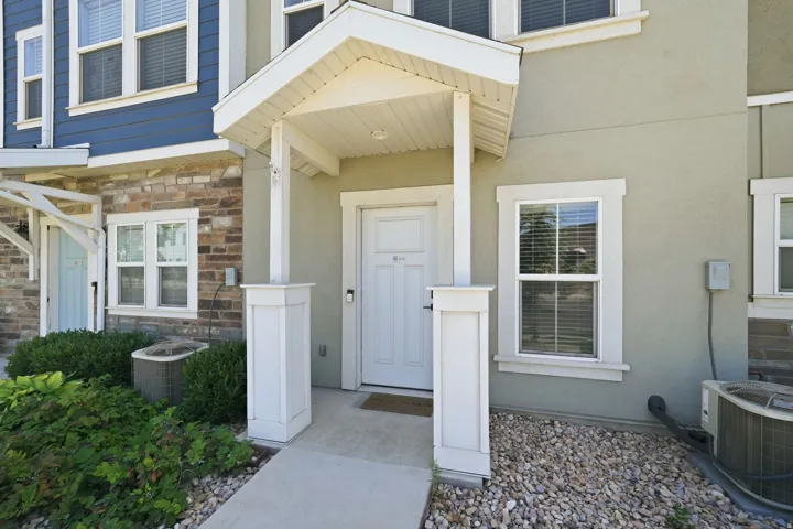 Covered entry with white columns and a white door, featuring light stucco and stone veneer siding, and a landscaped rock bed