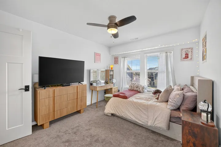 Bedroom featuring a ceiling fan with integrated lighting, dual windows with blinds, and white panel doors