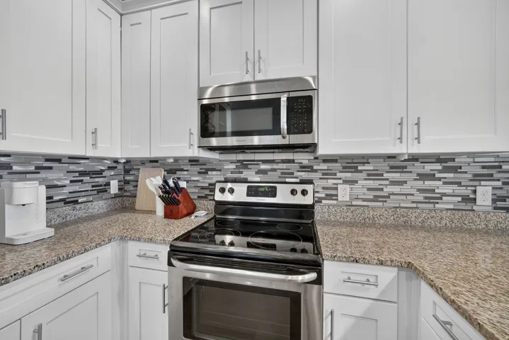 Kitchen featuring white shaker cabinetry, stainless steel oven/range, built-in microwave, granite countertops, and a glass tile backsplash